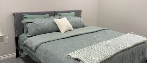 A modern bedroom with a bed, grey bedding, and a grey floor.