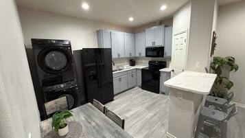 Una cocina funcional con lavadora, refrigerador, microondas y un pequeño comedor con mesa y sillas.