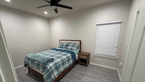 A bedroom with a bed, a nightstand, a ceiling fan, and a window with blinds.