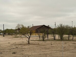 A fenced area with sparse vegetation and a single building with a metal roof.
