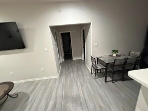Ein Zimmer mit Esstisch und Stühlen, einem an der Wand befestigten Fernseher und einer Tür zu einem anderen Raum.
