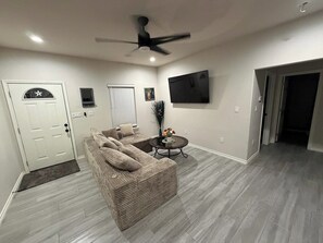 A living room with a sofa, a coffee table, a ceiling fan, and a flat-screen TV mounted on the wall.