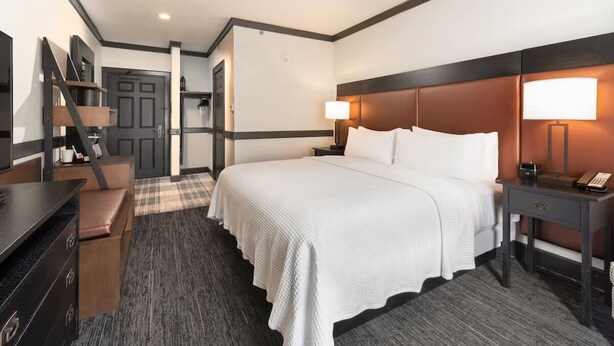 A hotel room with a large bed, a desk, a chair, a wardrobe, and a door leading to another room.