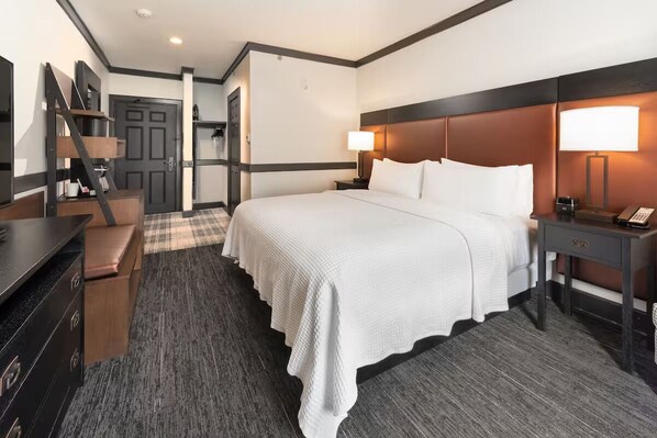 Habitación de hotel con una cama grande, un escritorio, una silla, un armario y una puerta que da a otra habitación.