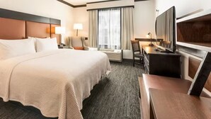 A hotel room with a large bed, a desk with a chair, a television, and a window with curtains.