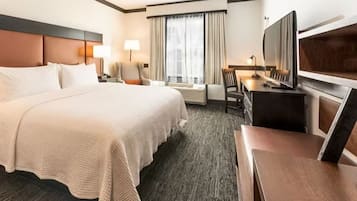 Une chambre d’hôtel avec un grand lit, un bureau avec une chaise, une télévision et une fenêtre avec des rideaux.