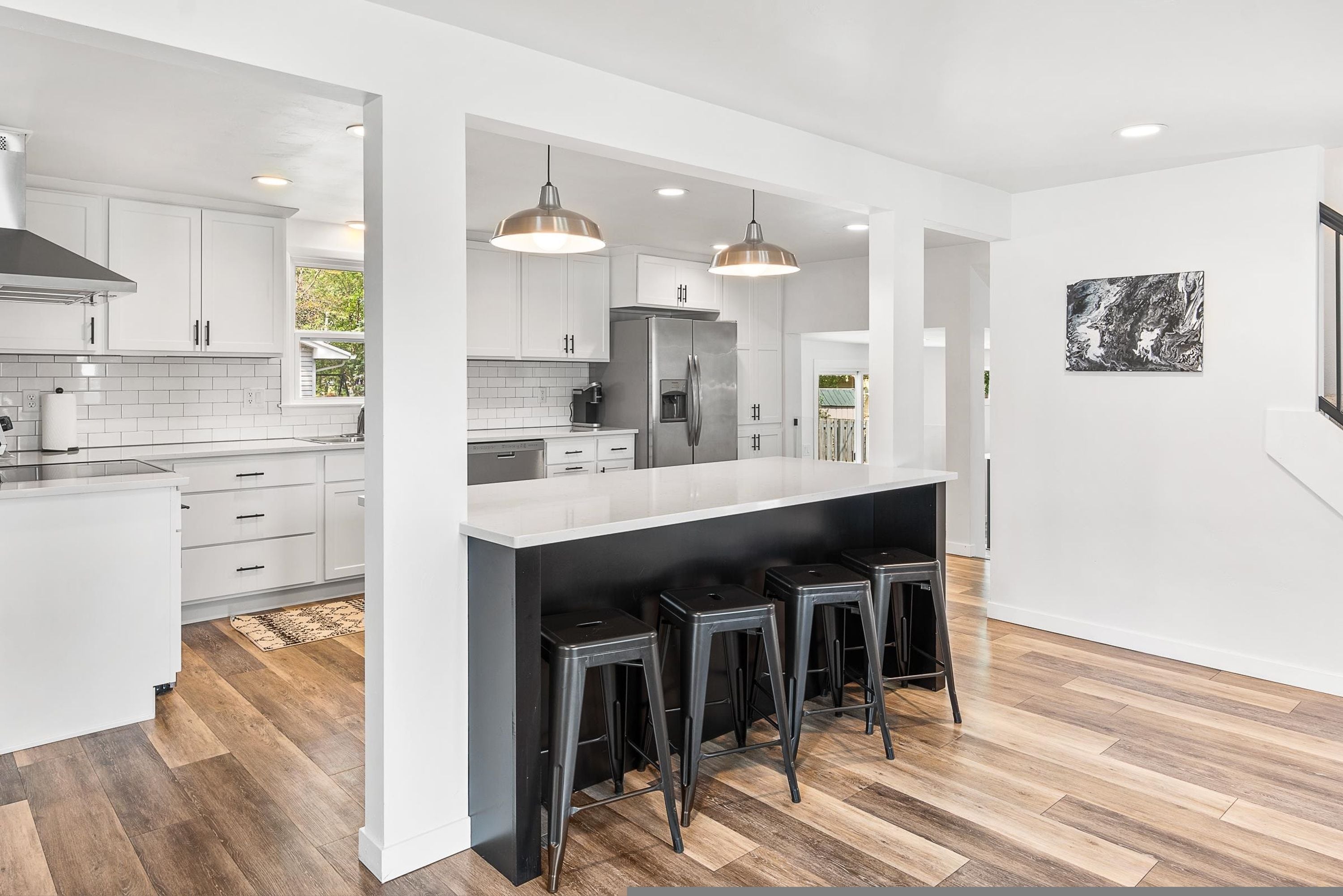 A modern kitchen with white cabinetry, a central island with bar stools, and pendant lighting.