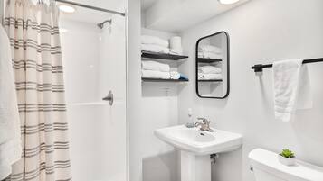 Un baño con ducha, lavamanos, inodoro y espejo.