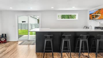 A modern kitchen with a central island, bar stools, recessed ceiling lights, and a view of the outdoors.