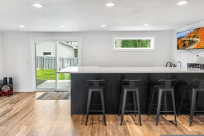 Cozinha moderna com ilha central, banquetas, iluminação embutida no teto e vista para o exterior.