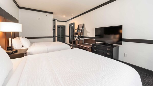 Ein Hotelzimmer mit zwei Betten, einem Schreibtisch, einem Sessel, einem Fernseher und einer Lampe.