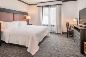 A hotel room with a large bed, a desk with a chair, a dresser, and a window with curtains. - Spacious Signature Suite at The Craftsman Inn | Pet Friendly (FAYETTEVILLE)