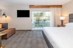 Een hotelkamer met een bed, een bank, een televisie, een lamp en uitzicht op groen.