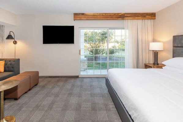 Ein Hotelzimmer mit Bett, einer Couch, einem Fernseher, einer Lampe und Blick auf Grünflächen.