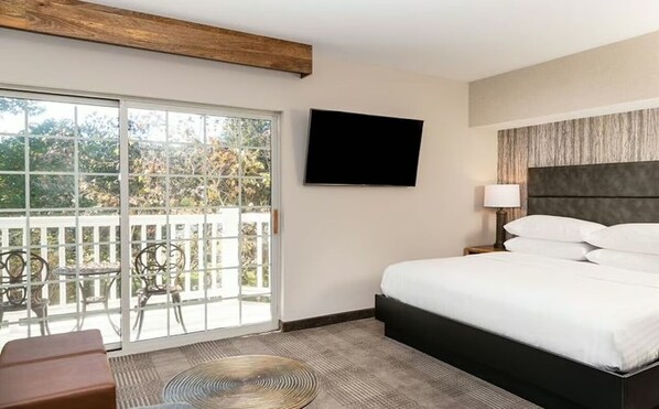 Een hotelkamer met een bed, een televisie, een balkon met stoelen en uitzicht op bomen.