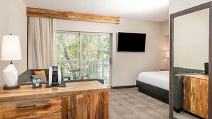 Ein Hotelzimmer mit einem Holztisch, einem Bett, einem Fernseher und Blick ins Freie.
