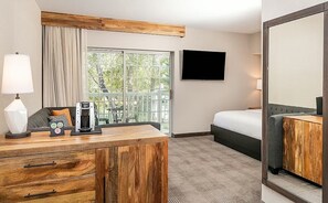 Een hotelkamer met een houten bureau, een bed, een televisie en uitzicht op het groen.