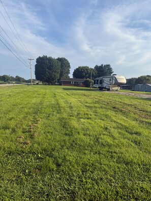 A grassy field with a large RV and a building in the background.