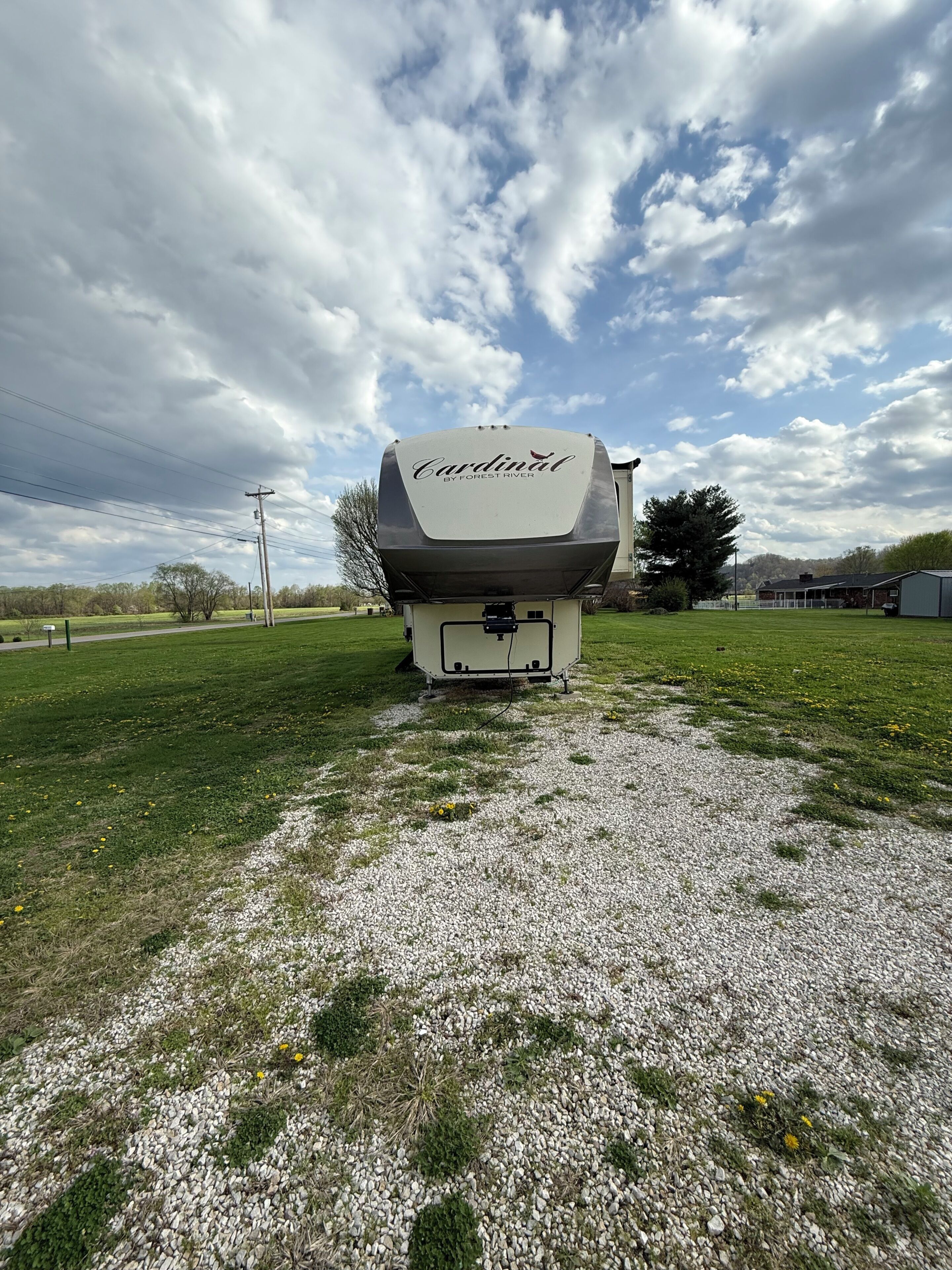 Un véhicule récréatif (VR) doté d’un espace de rangement couvert, portant l’inscription « Cardinal by Forest River », est stationné sur une surface de gravier dans un champ herbeux.