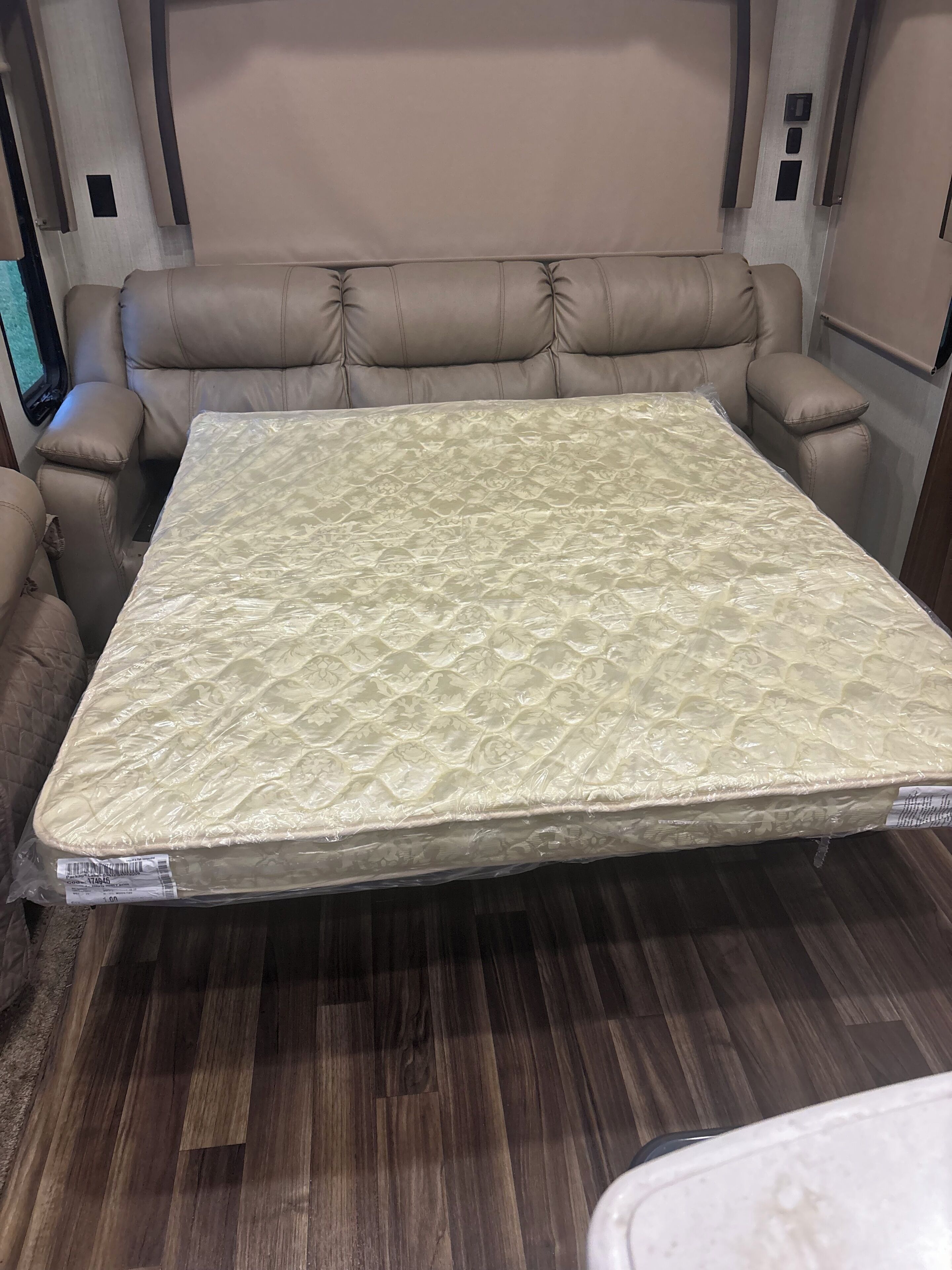 A bed with a patterned mattress in a room with wooden flooring and beige walls.