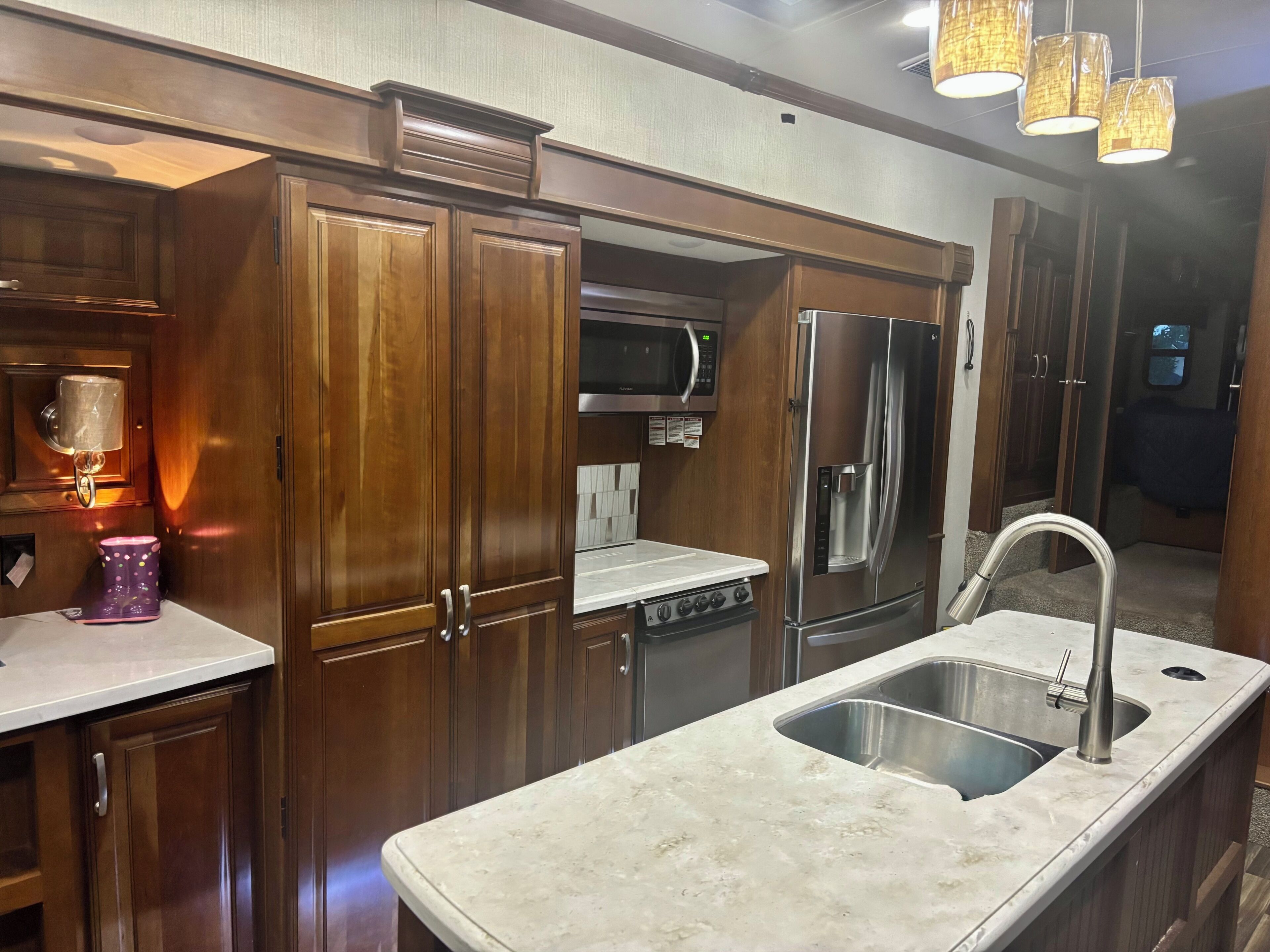 Cocina compacta con gabinetes de madera, un refrigerador de acero inoxidable, un microondas y un lavamanos.