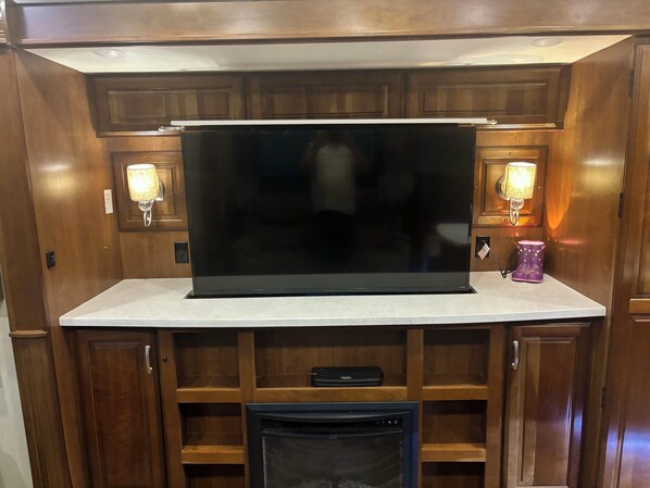 A kitchen with a large black flat-screen TV, wooden cabinets, and two wall-mounted lamps.