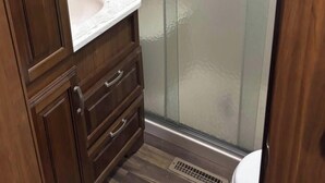 Une salle de bain avec un meuble-lavabo en bois, une cabine de douche en verre et des toilettes.
