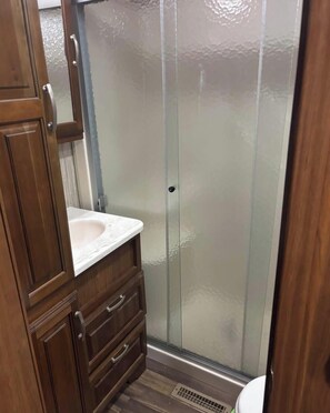 A bathroom with a wooden vanity, a glass shower enclosure, and a toilet. - Cozy All Season 5th wheel camper in tranquil Greenup, ky. (Greenup)