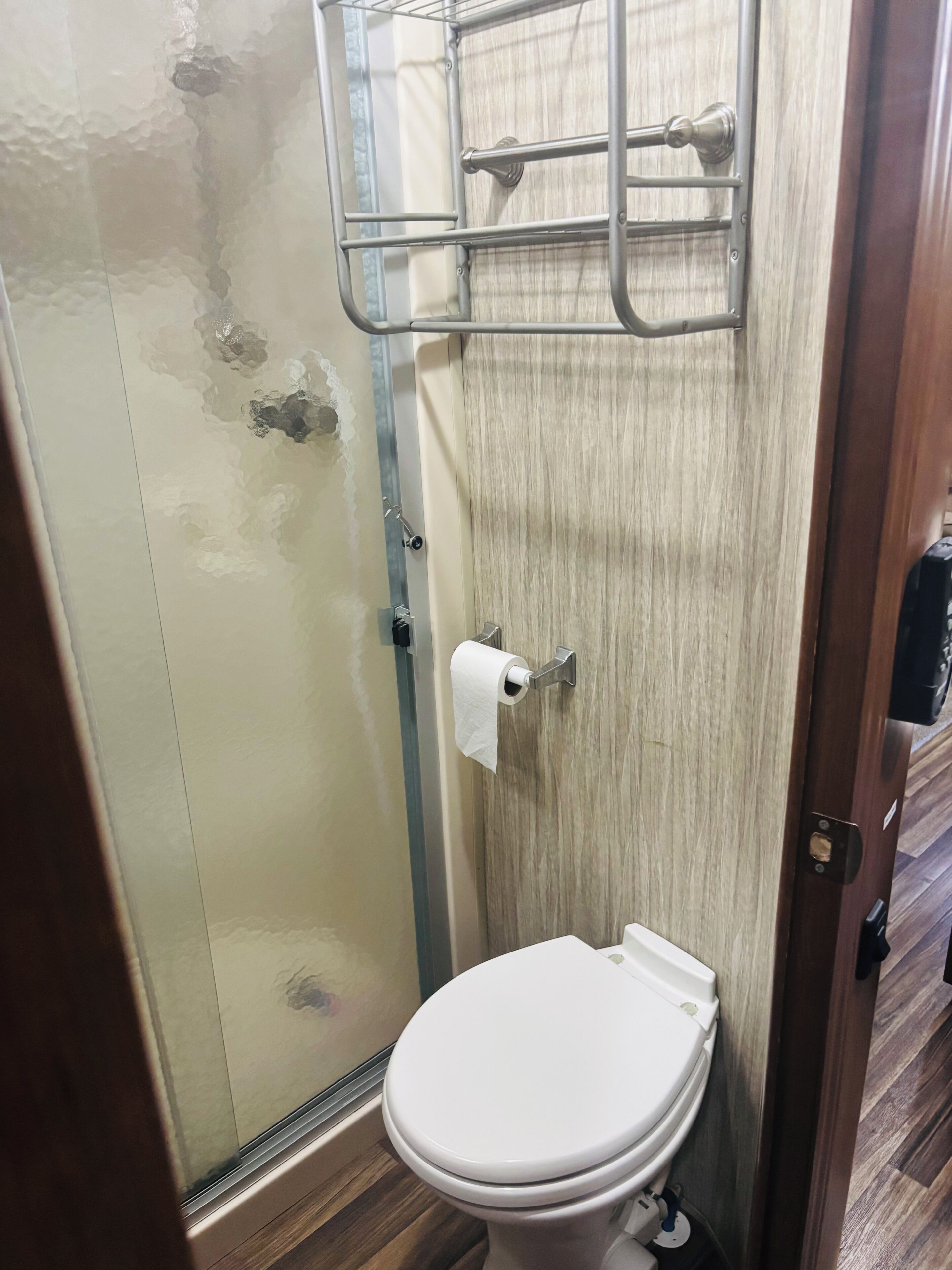 A bathroom with a glass shower enclosure, a toilet, and a towel rack.