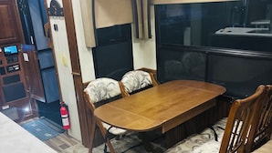 Un espace repas comprenant une table et des chaises en bois, un extincteur, ainsi qu’un coin cuisine avec une cuisinière et des placards.