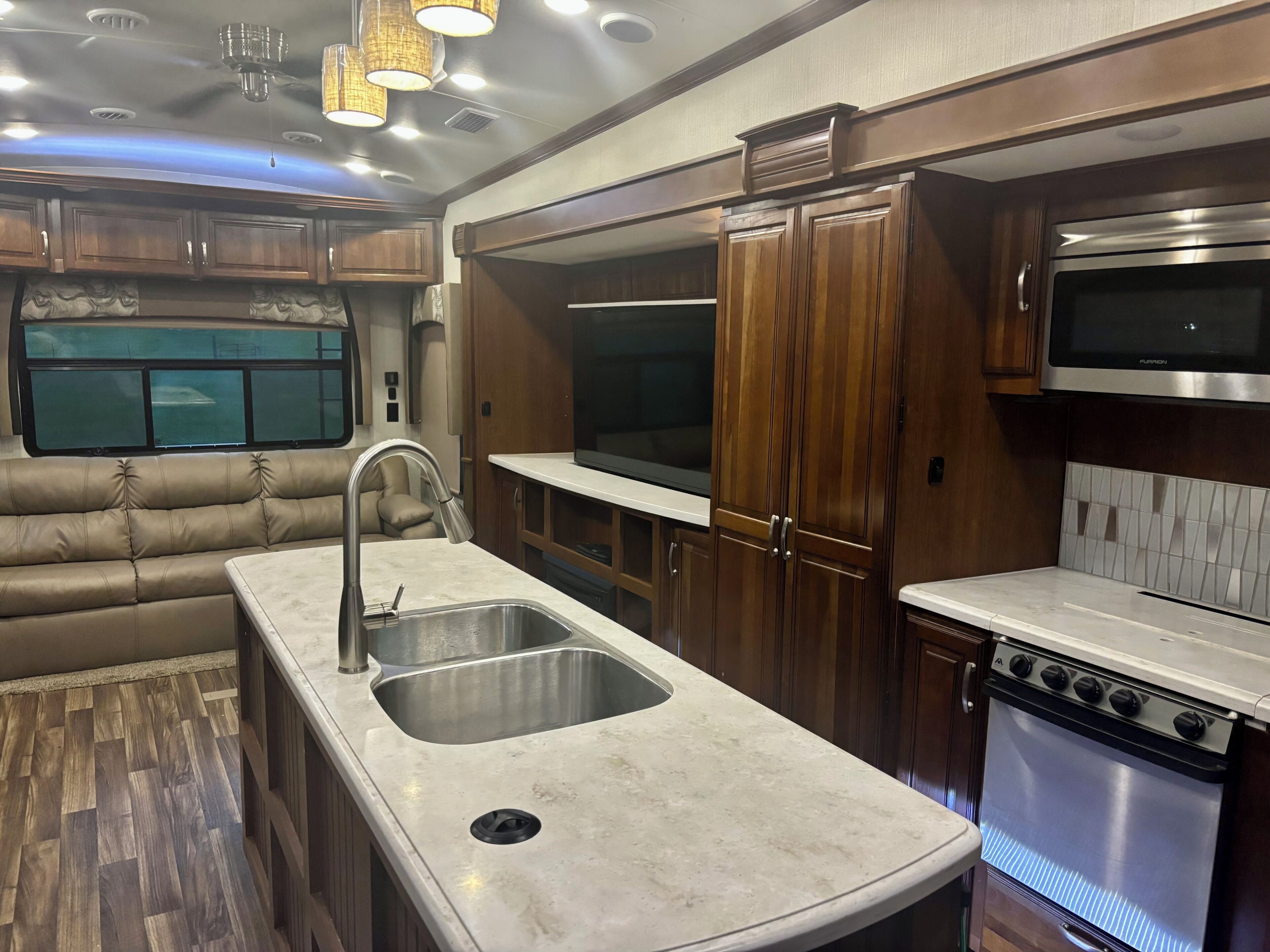 A compact RV kitchen with a sink, stove, and wooden cabinets.