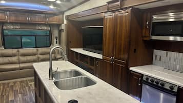 A compact RV kitchen with a sink, stove, and wooden cabinets.