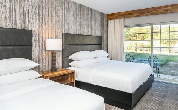 Habitación de hotel con dos camas, una mesita de noche, una lámpara y un ventanal con vistas al exterior.