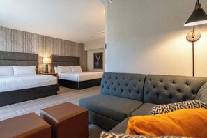 Ett hotellrum med två sängar, en grå soffa och en lampa.