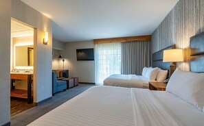 Een hotelkamer met twee bedden, een bureau, een stoel, een lamp en een groot raam met gordijnen.