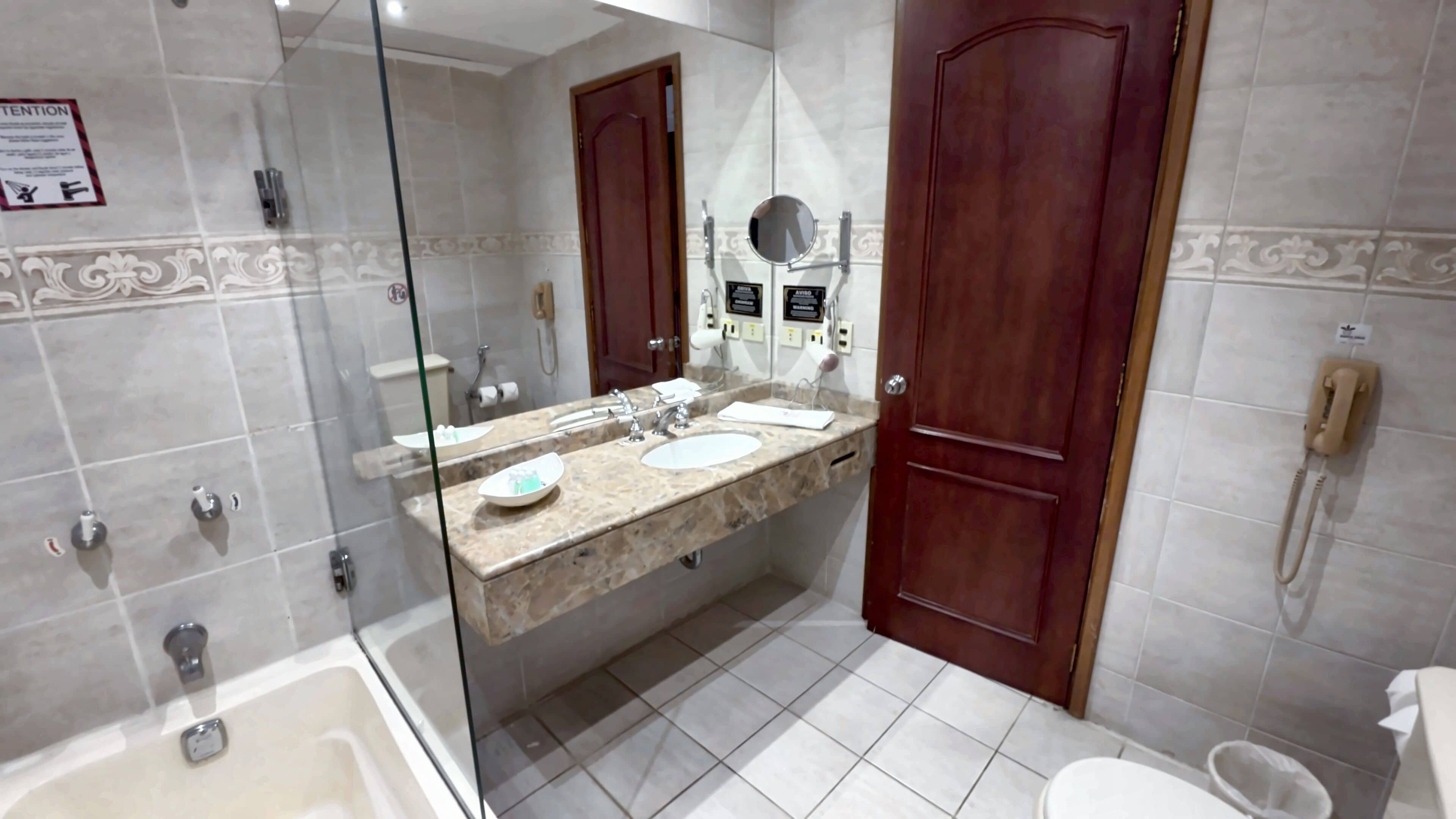 A bathroom with a glass-enclosed shower, a double sink vanity, a toilet, and a telephone.