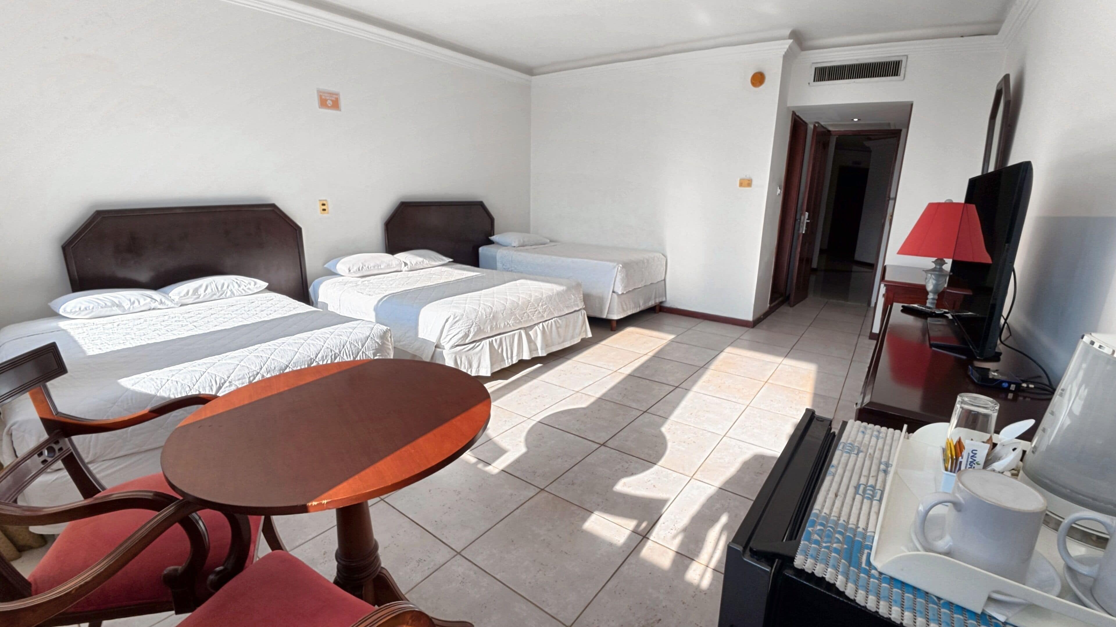 A hotel room with two beds, a desk, a chair, a television, and a lamp.