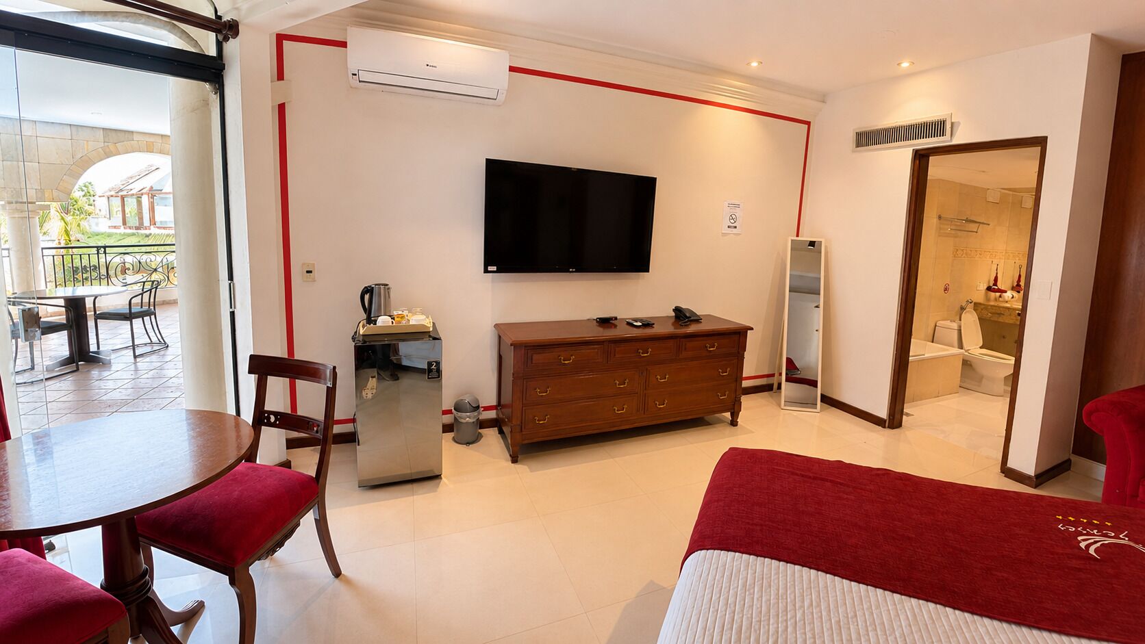A hotel room with a dining area, a television, a minibar, and a bathroom visible through an open door.