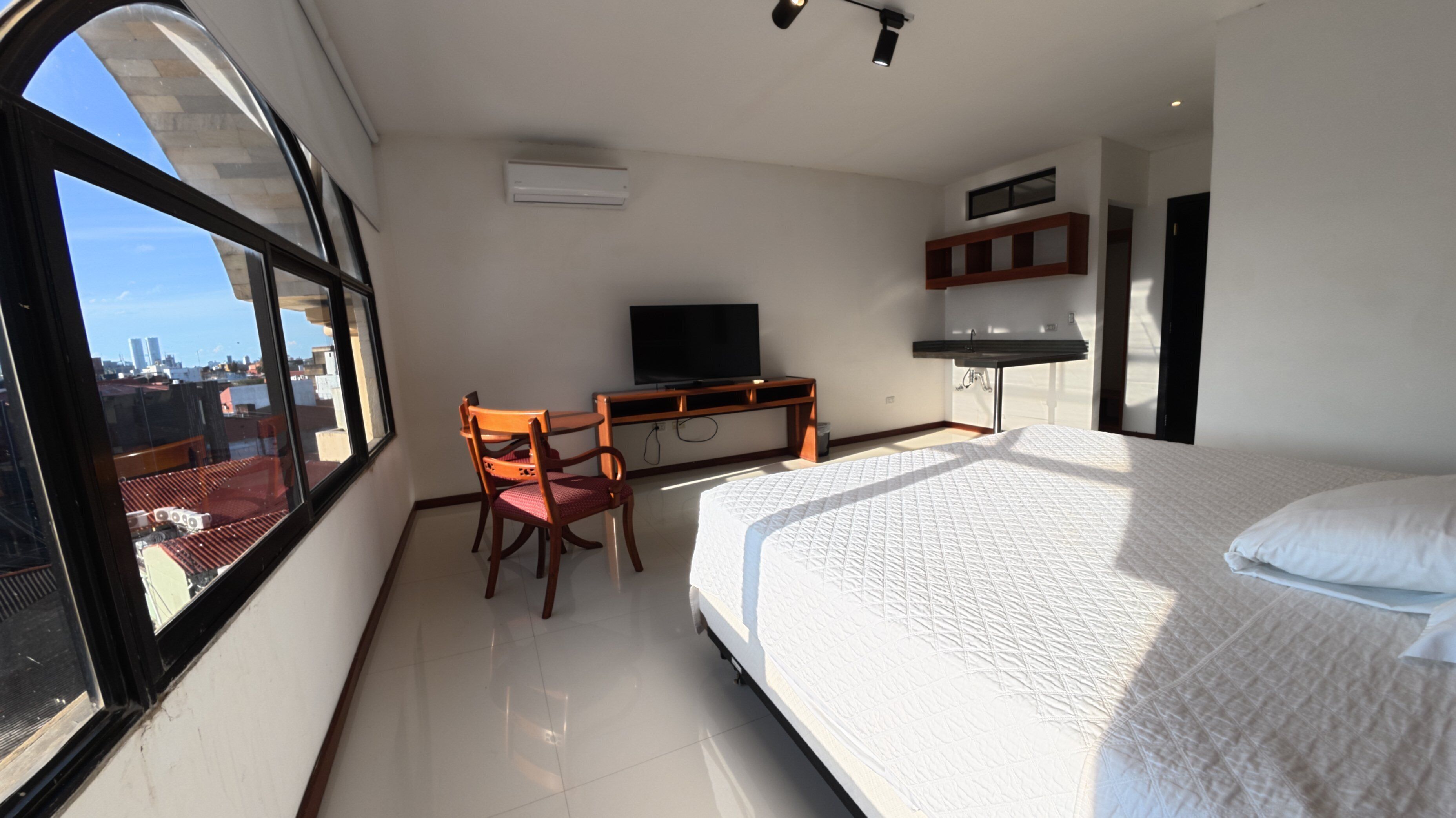 Habitación de hotel con cama, escritorio con silla, televisión y ventana con vista a la ciudad.
