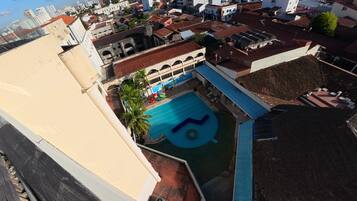 Vista aérea de uma área residencial com piscina, parquinho e um edifício grande com telhado vermelho.