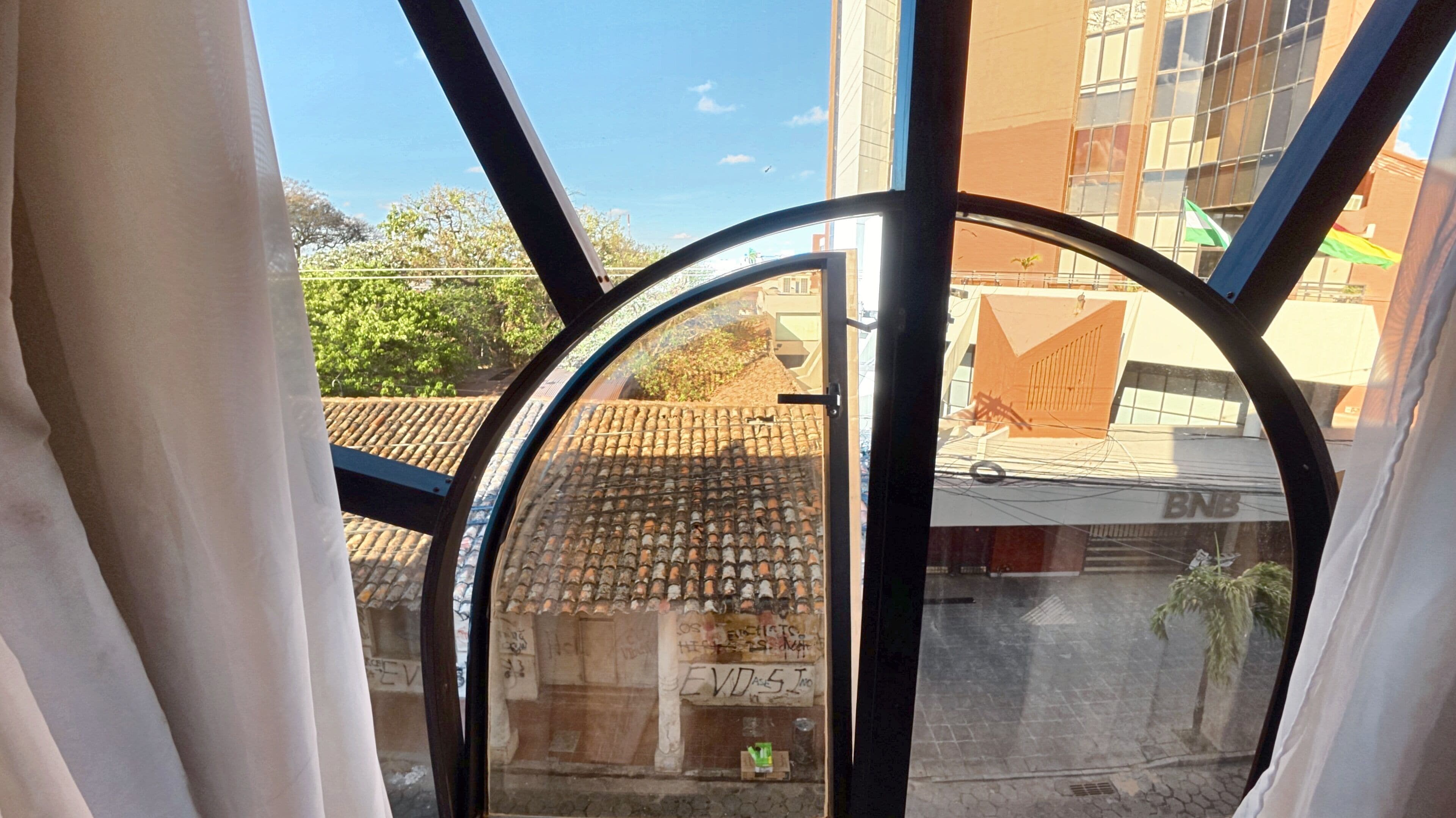 A view through a window with a metal frame, a tiled roof, and a building with a sign that reads 'BNB'.