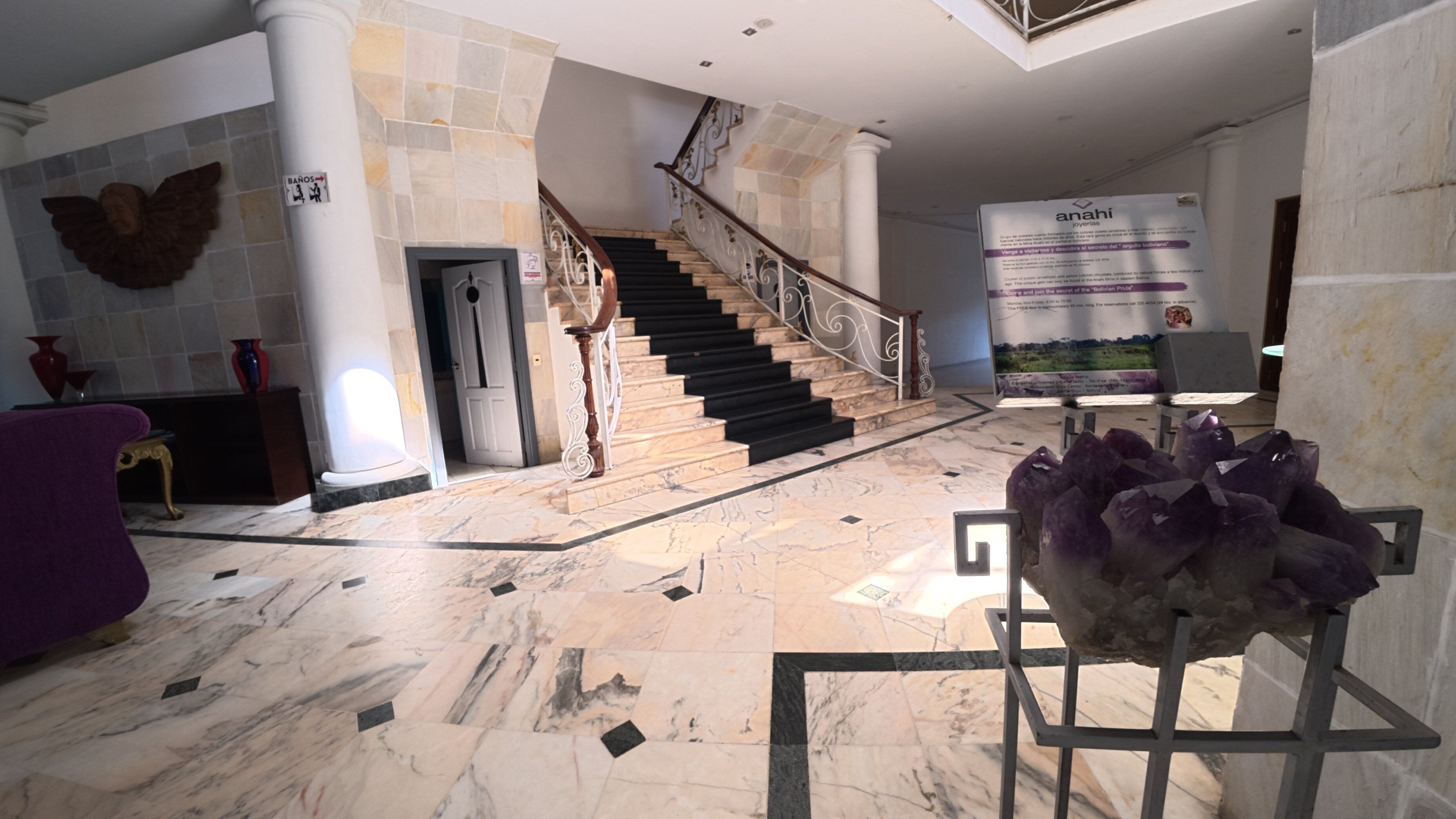 A marble-floored lobby with a staircase, a large crystal sculpture, and a banner.
