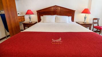 A hotel room with a large bed, two bedside tables with lamps, a wooden headboard, and a red carpet with a logo.