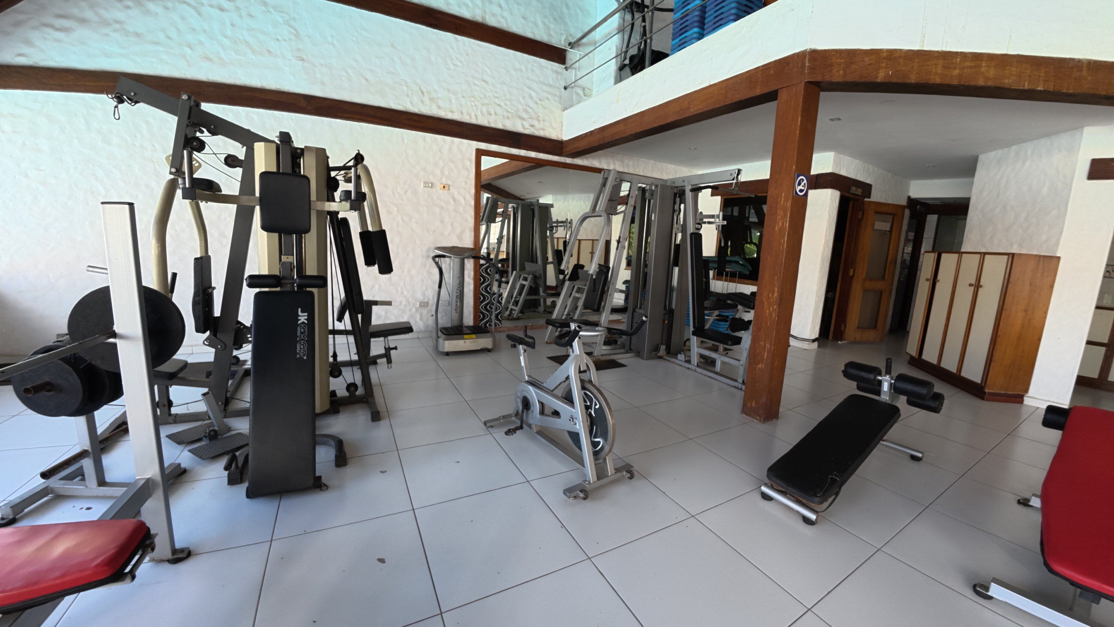 A gym with various exercise equipment, including weight machines and cardio machines, and a red exercise bench.