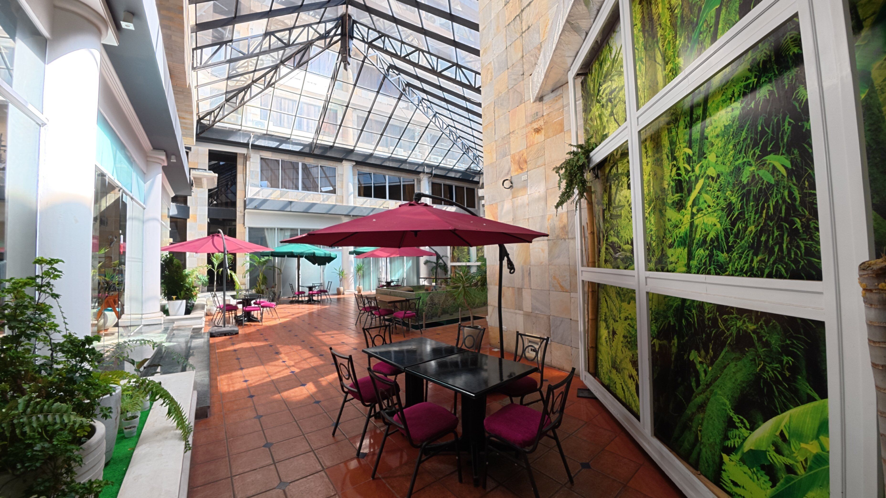 Un patio interior con techo de vidrio, sombrillas rojas y una mesa de comedor con sillas.