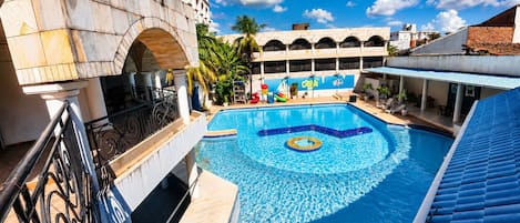 A swimming pool with a decorative center, surrounded by a building with a blue roof and a mural.