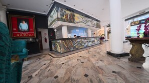Un vestíbulo con mostrador de recepción, un retrato enmarco, un sillón turquesa y piso de mármol.