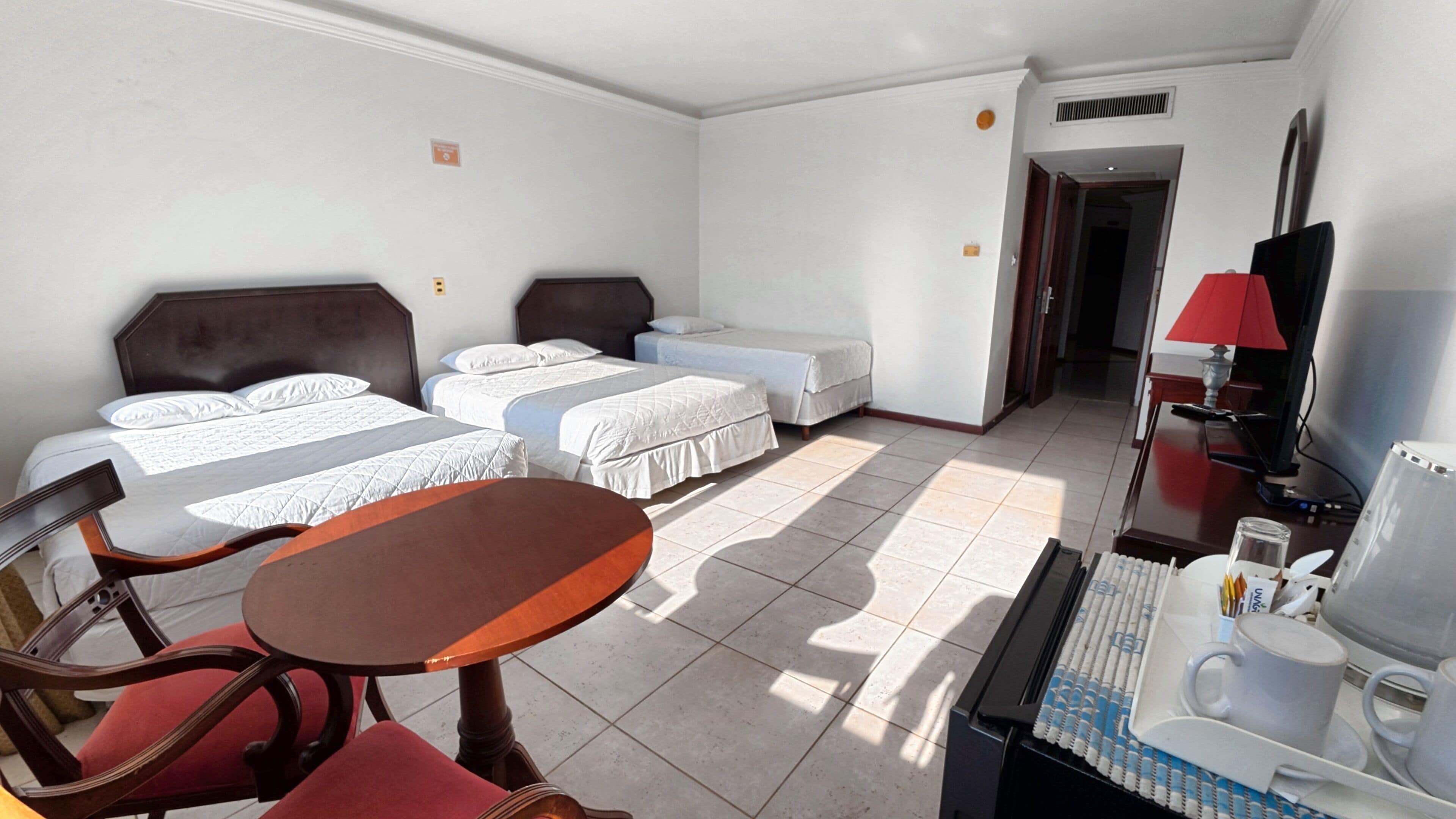 Una habitación de hotel con dos camas, una mesa de comedor, un televisor y un escritorio con lámpara.