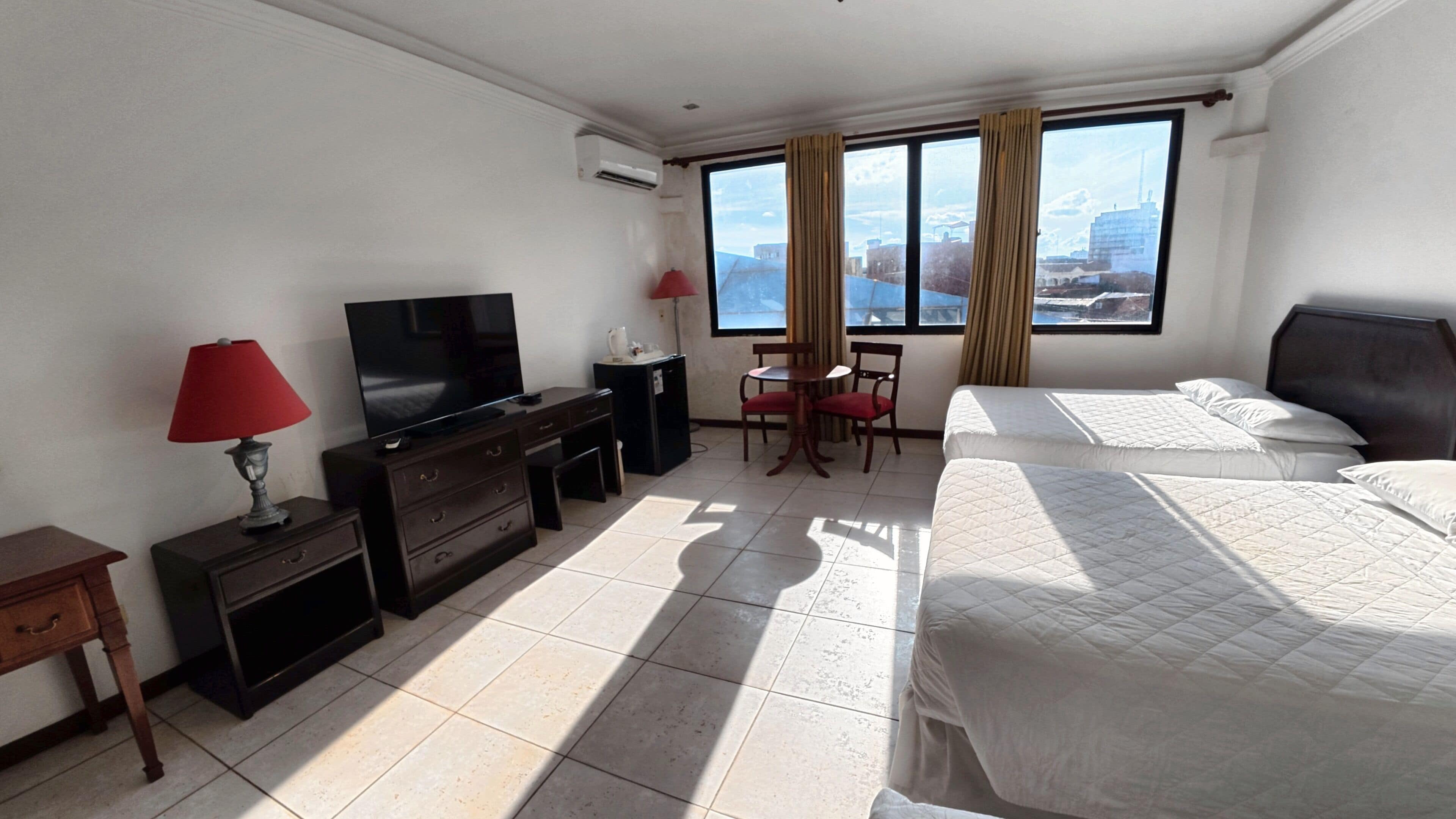 Een hotelkamer met een bed, een televisie, een bureau met lamp, een stoel en een raam met uitzicht.