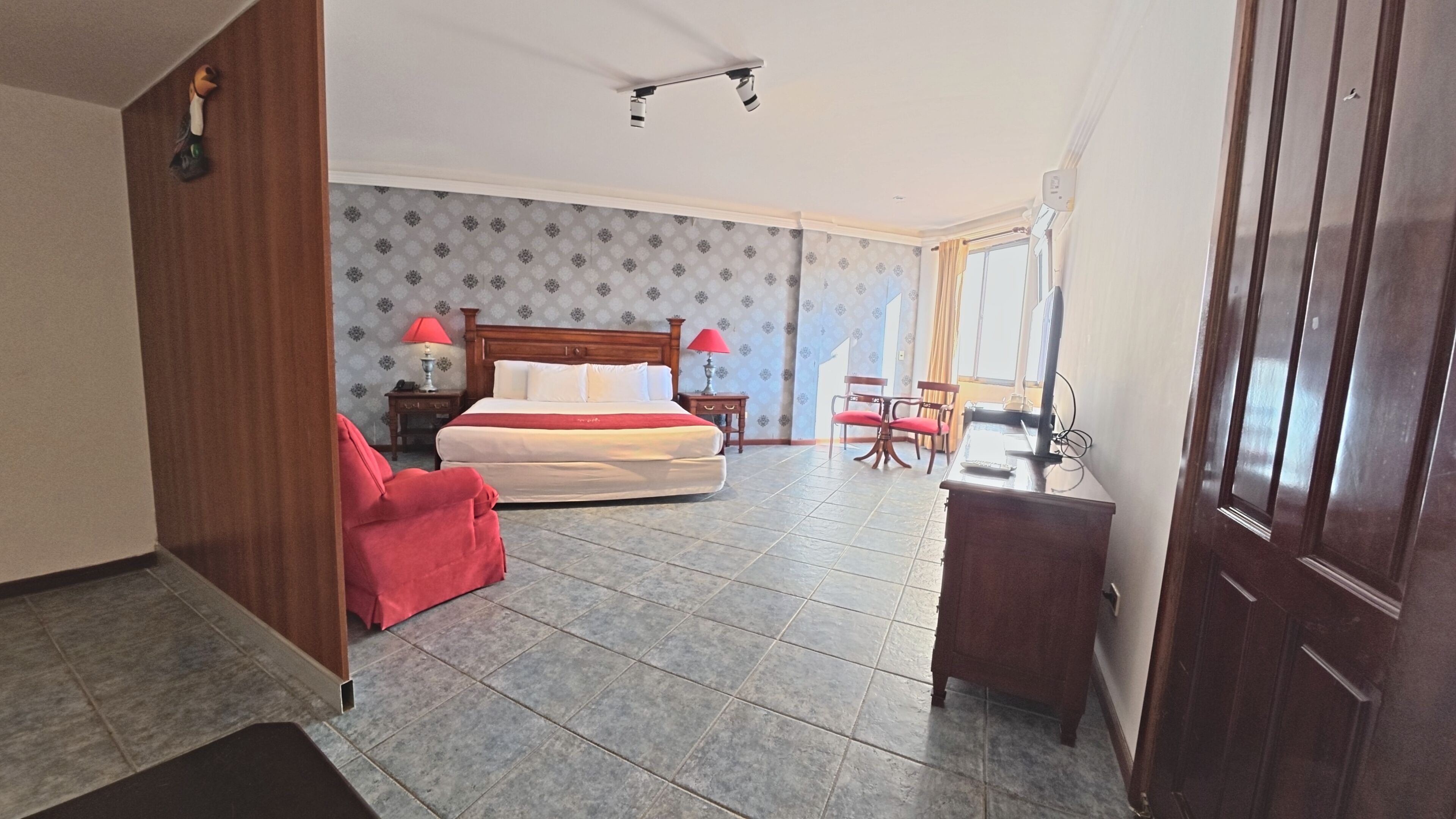 Una habitación de hotel con cama, escritorio, silla, lámpara y ventana.